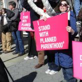 Protesters holding banners. One says I Stand with Planned Parenthood, another one says "Don't take away my birth control"