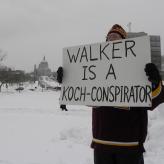 A man in winter clothes holding a board that says "walker is a koch-conspirator"