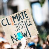 A protestor's hand holding a sign that says, "Climate Justice Now!"