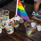 A table with plastic cups that have stickers on them that say "Pride." One of the cups has a rainbow flag in it.