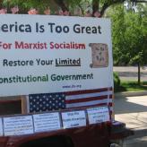 A sign that says "America is too great for marxist socialism. Restore your limited. Constitutional Government. www.jbs.org"