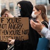 A person holding a sign that says "If you're not angry, then you're not listening."