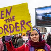 A woman with a scarf holding a sign that says "open the borders"