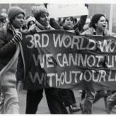 Four people walking holding a banner that says "3rd world women we cannot live without our lives"