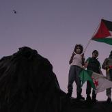 Four people carrying a Palestinian flag standing on a lion.