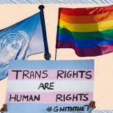 A UN flag, an LGBT flag and a sign that says "Trans rights are human rights"