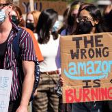 A person wearing a mask holding a sign saying "The wrong Amazon is burning"