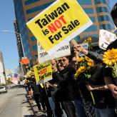 people standing in a row holding sunflowers. A sign says "Taiwan is not for sale."
