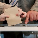 a person dropping an envelope into a ballot box.