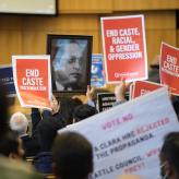 People holding banners that say "End Caste Discrimintaion" and "End Caste, Racial, And Gender Opression" and a picture of Dr. Ambedkar.