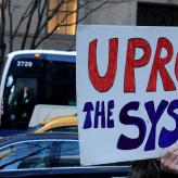 A person holding a sign that says "uproot the system"