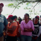 A group of people wearing red hats led by a man speaking with his hand raised. 