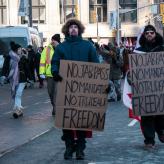 Two people in winter clothes holding signs that say "No jab pass, no mandates, no Trudeau, Freedom"