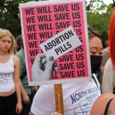 a sign that reads "We will save us" over and over again with a hand that holds a paper that says "Abortion Pills"