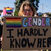 A sign at a protests saying "Gender? I hardly know her"