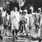 a black and white photo on people marching on the street, wearing hats and dhotis