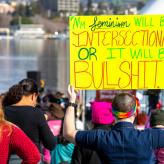 A person holding a yellow sign that reads "my feminism will be intersectional or it will be bullshit."