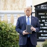 donald trump stands in front of a black sign for a church holding a bible in front of him