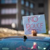 a person holding a sign out of the sunroof of their car that reads "no police state."