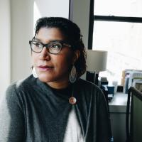 Ginna Green wears glasses and a steady gaze in bright office