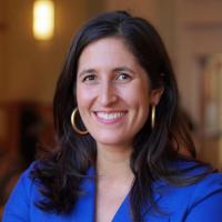 Smiling woman with brown hair, gold hoop earrings, and a bright blue blazer