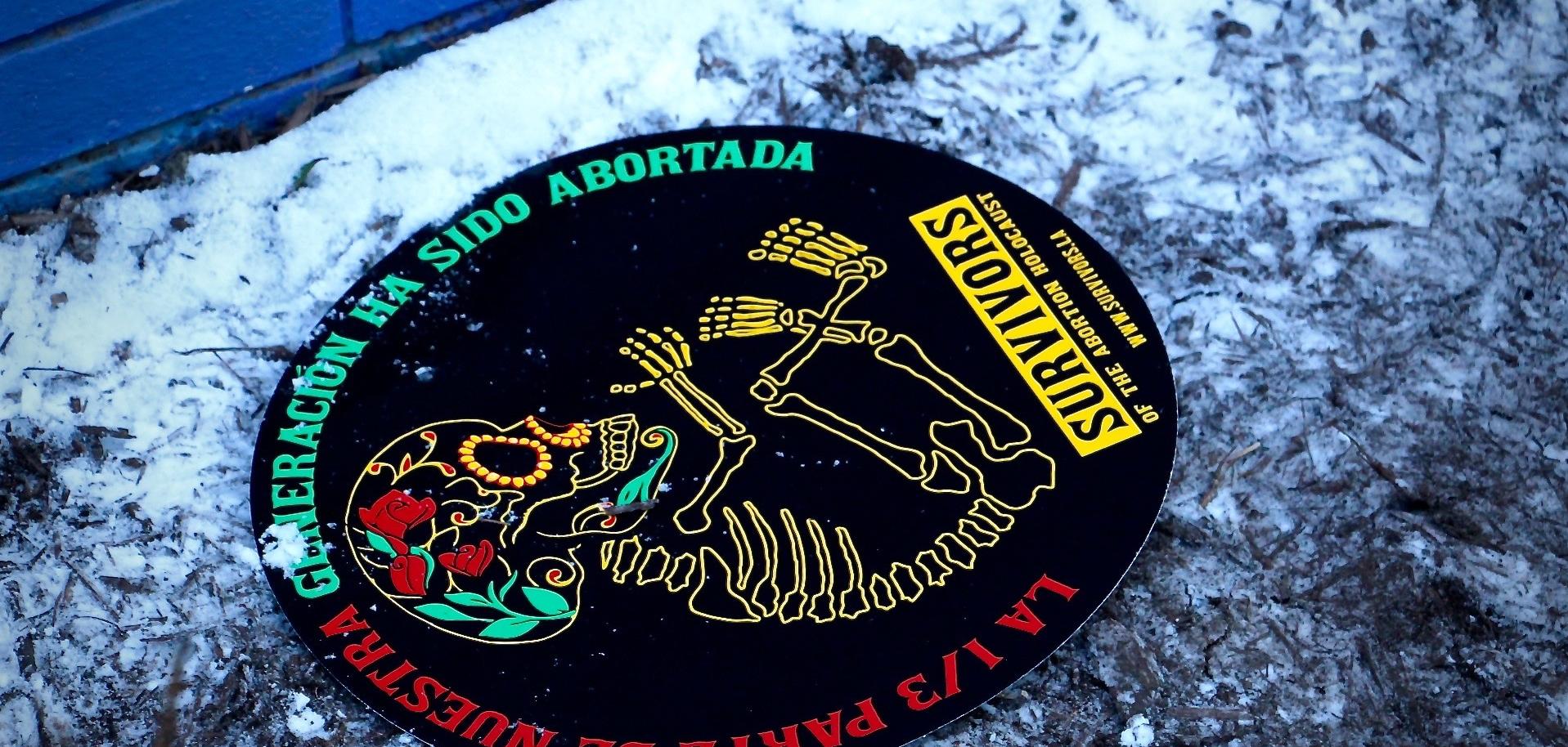 Sign left behind from an anti-abortion rally depicts dia de los muertes styled skeleton for abortion "survivors" network