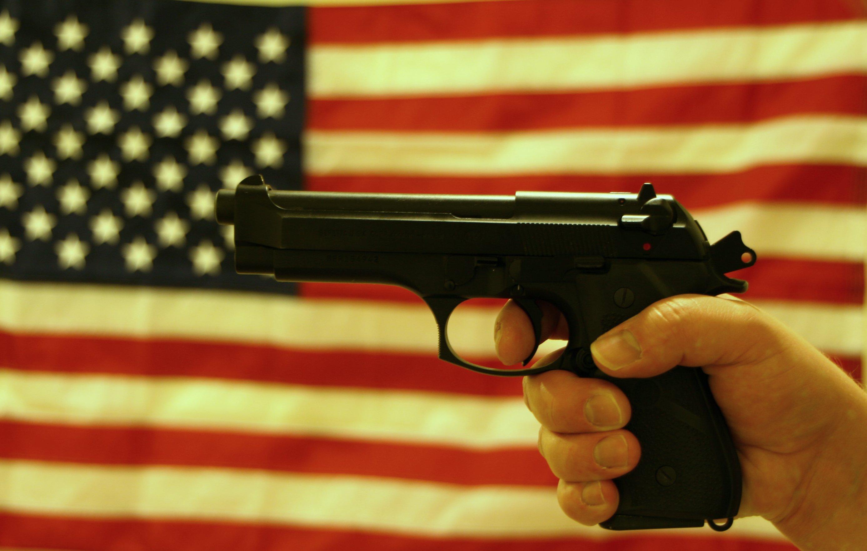 A hand gripping a handgun in front of an American flag backdrop