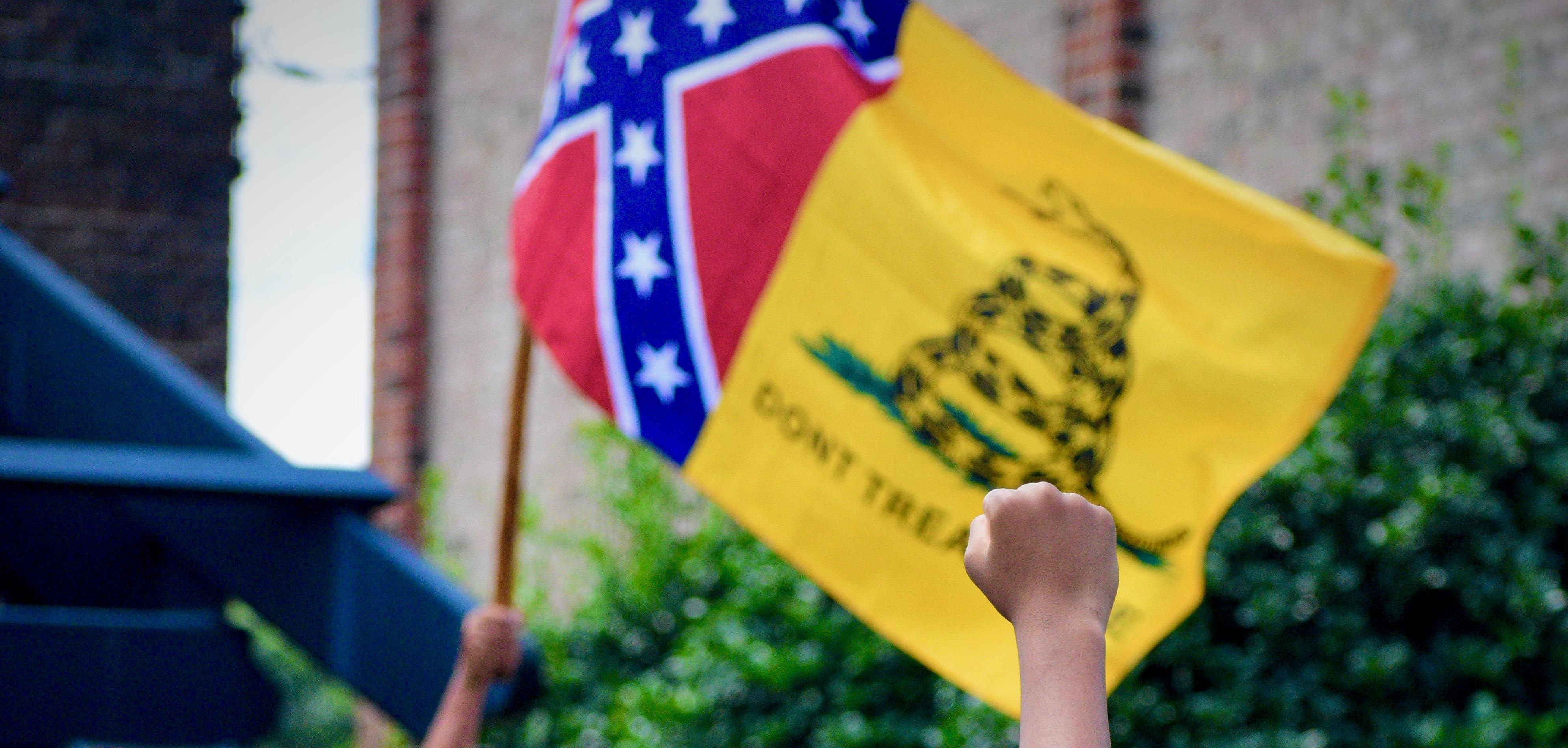 Pro-confederacy protestor holds up a confederate flag, a counter-protestor raises a fist in response. 