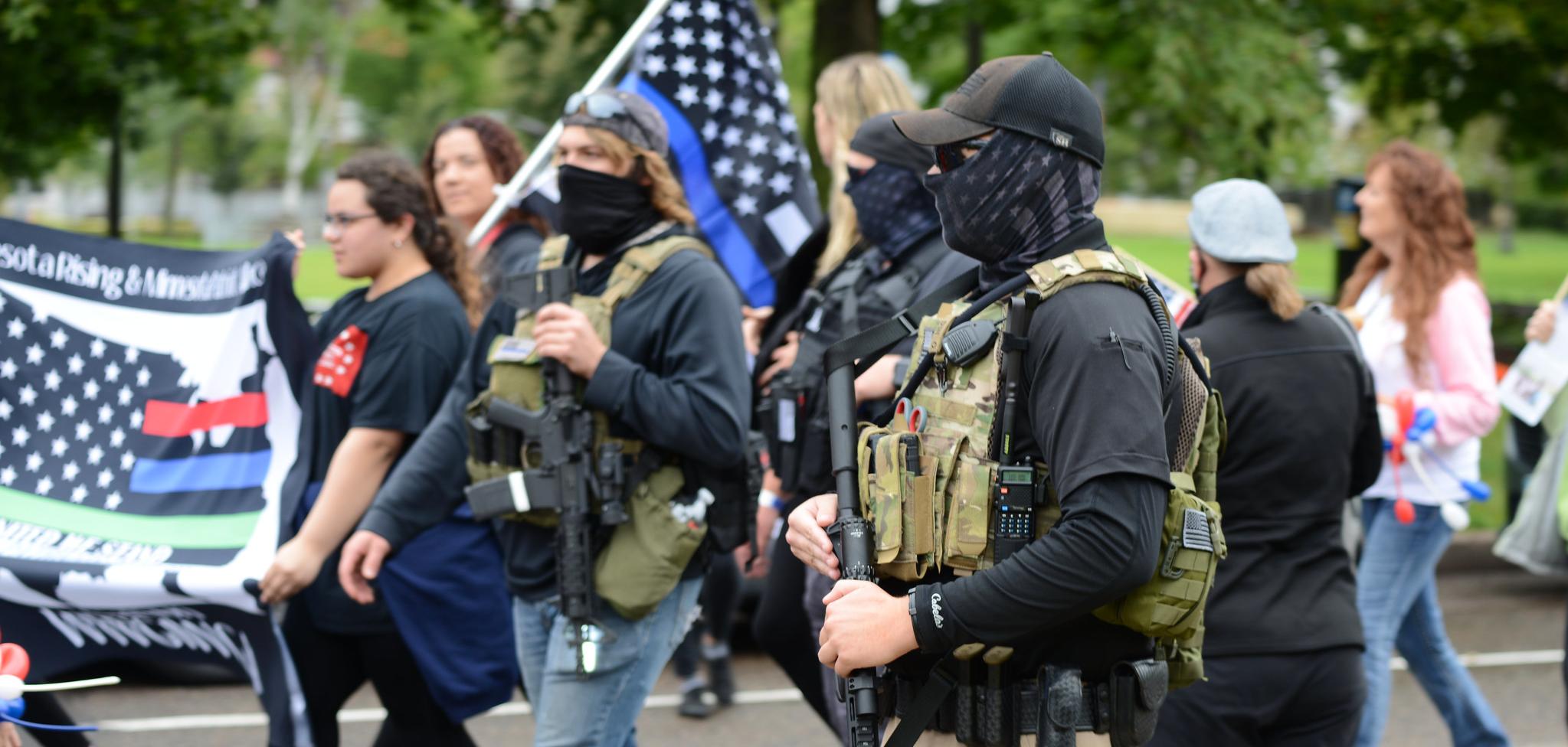 Armed militia members march next to a WWG1WGA flag, a common identifier of QAnon believers, at the United We Stand & Patriots March for America, St. Paul, Minnesota, September 12, 2020 (Credit: Fibonacci Blue/Flickr).