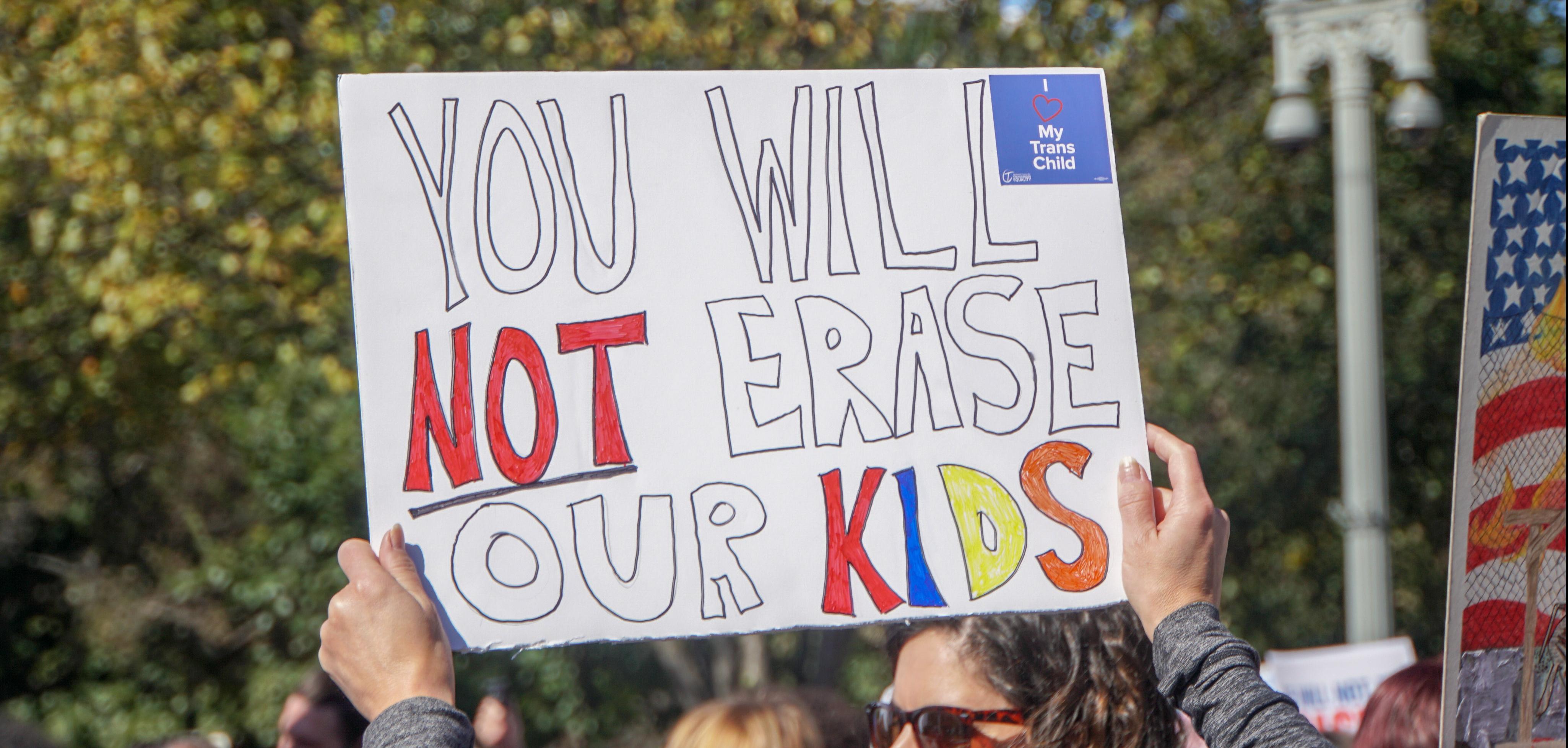 Hands holding up sign reading "You will not erase our kids"