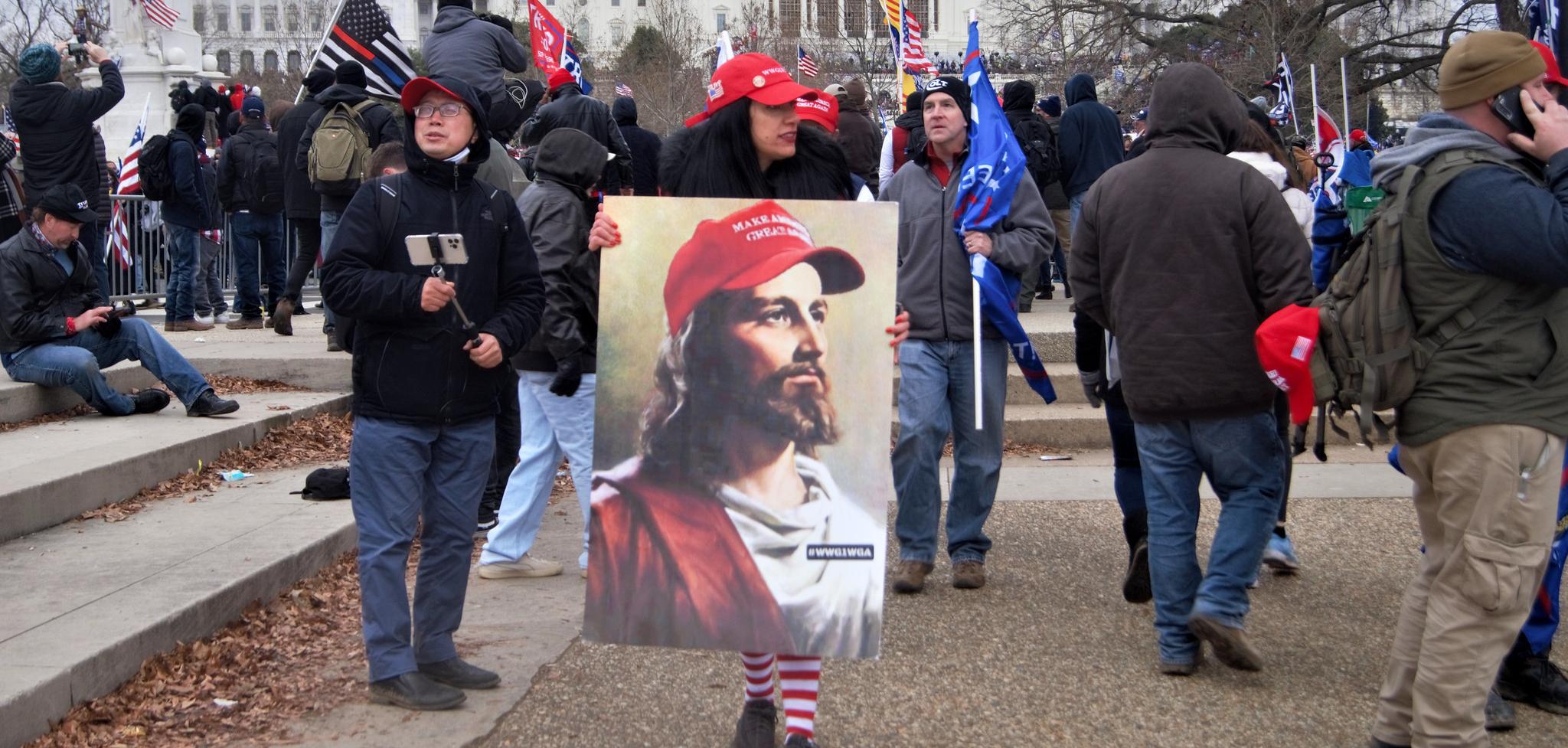 A woman wearing a red hat, holding a paining of Jesus wearing a Make America Great Again hat.