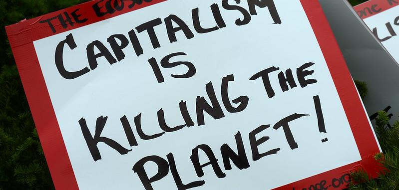 A red and white sign that says "capitalism is killing the planet!"
