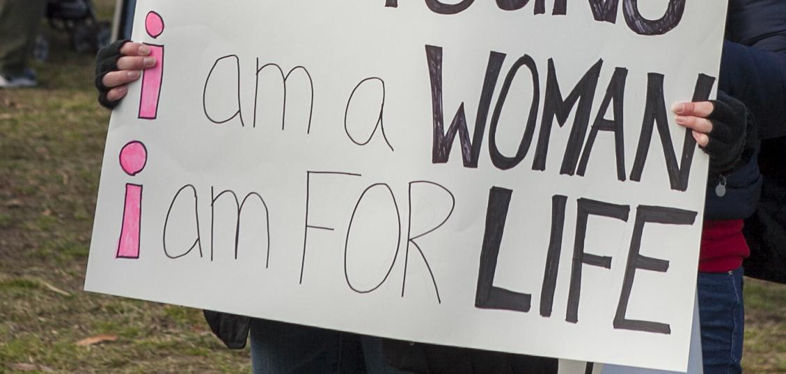 A white woman holding a sign saying "I am young, I am a woman, I am FOR life"