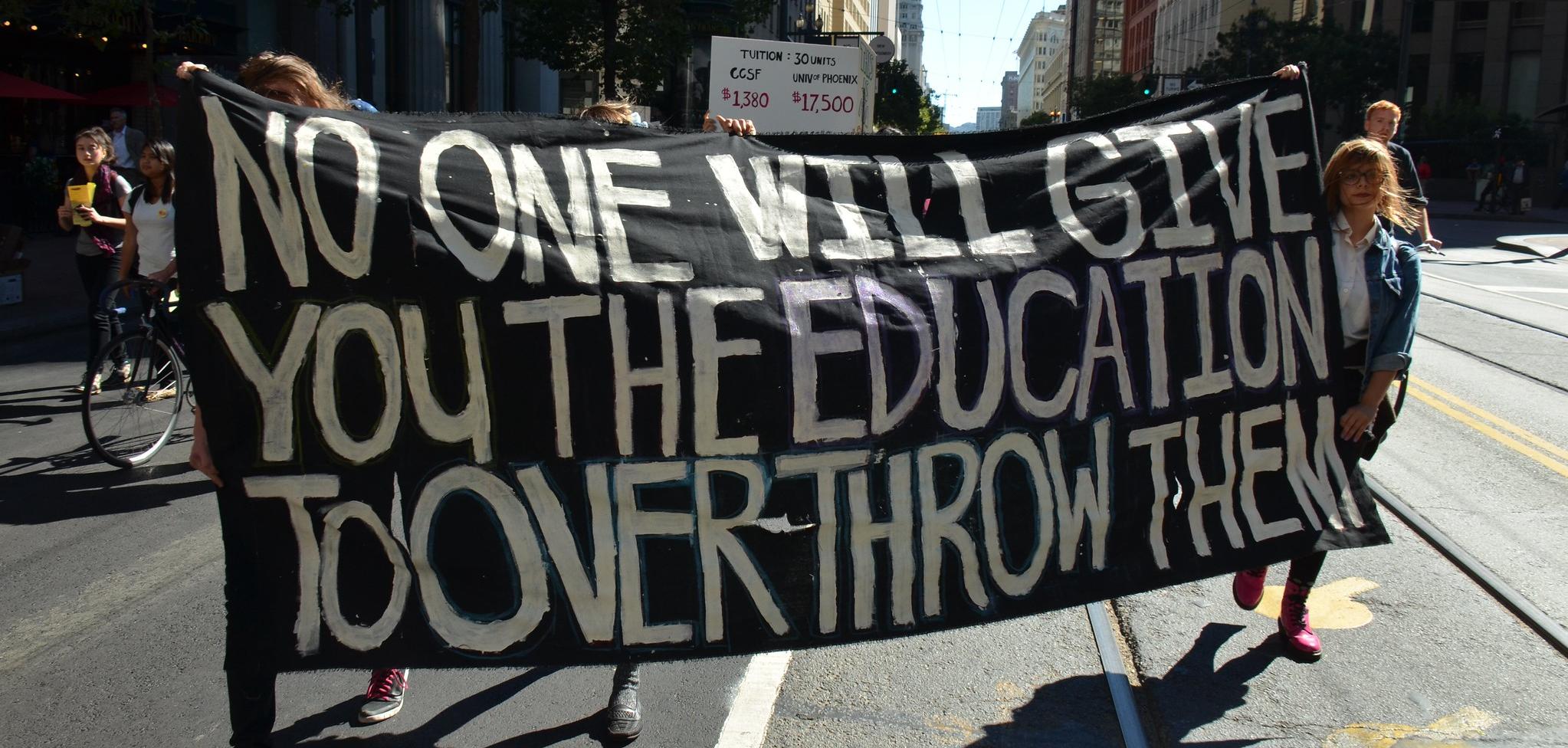 Protesters holding a banner that reads: No one will give you the education to overthrow them