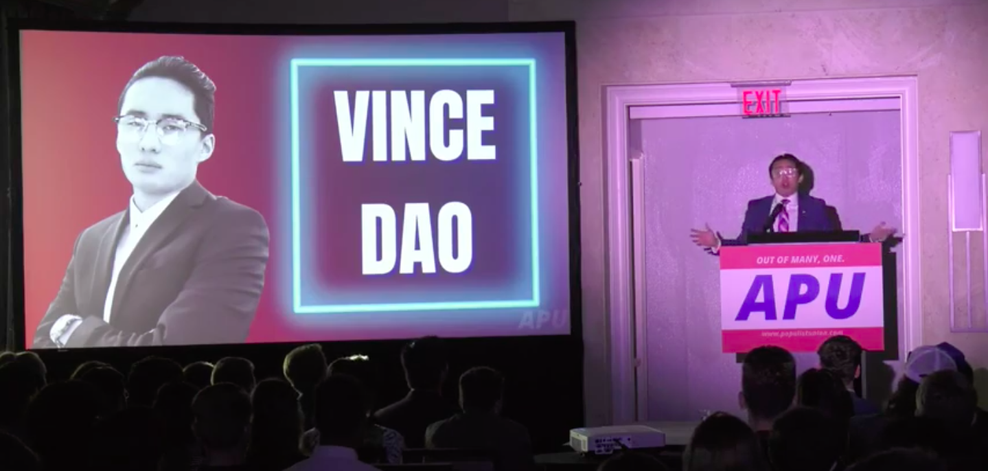 Man standing on stage next to Powerpoint that reads "Vince Dao"