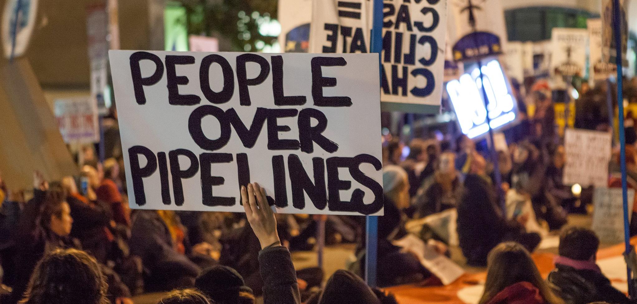 A protester holding a sign that reads "people over pipelines"