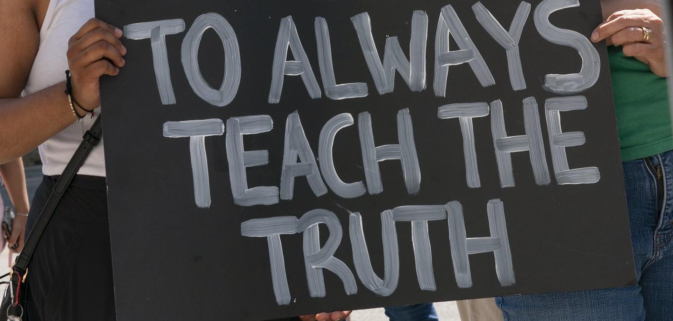 Woman holding sign that reads "I pledge to always teach the truth"