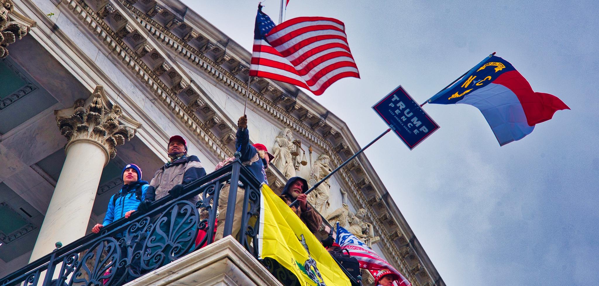 A U.S Flag, A Trump and Pence flag and other flags flying from the balcony of the Capitol building.