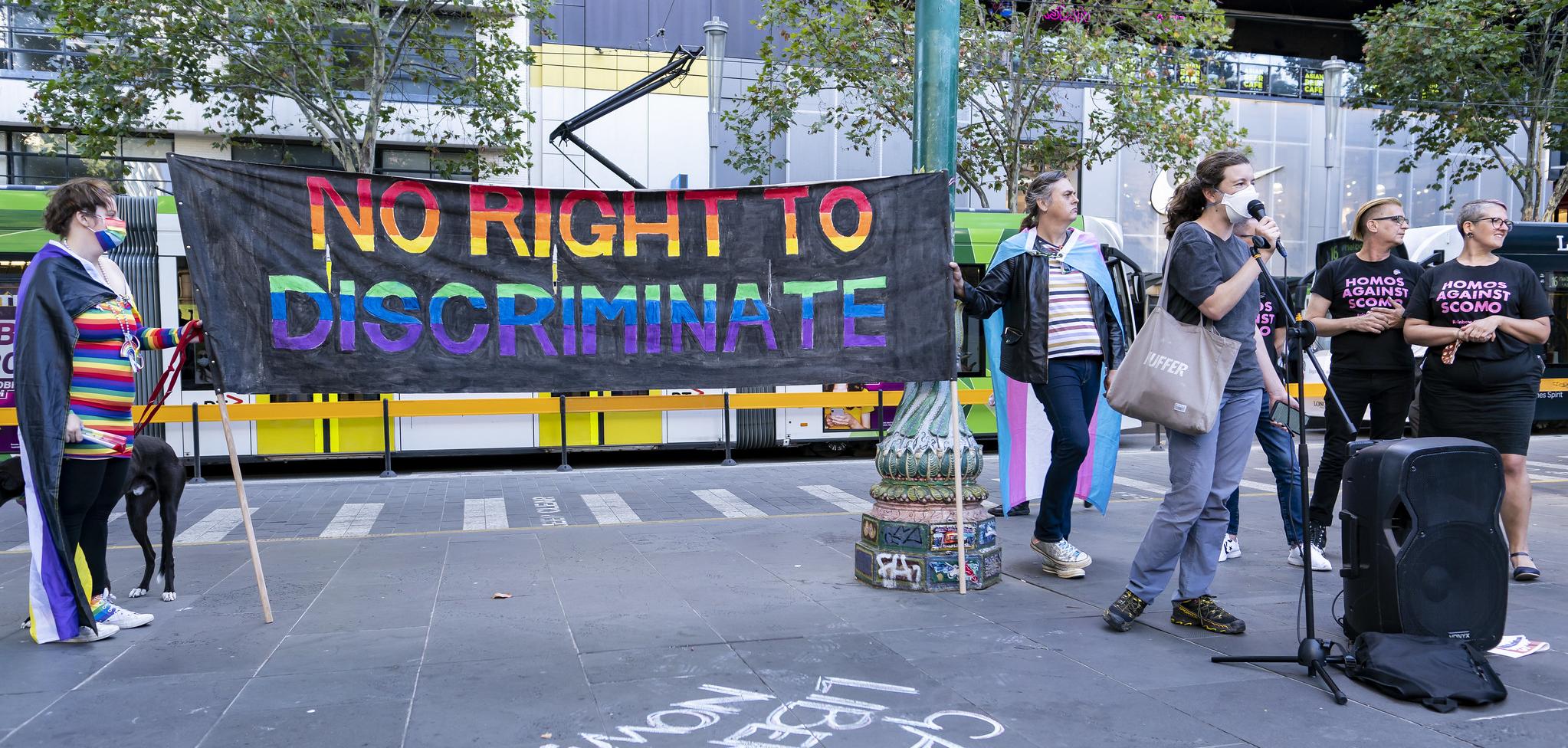 Protesters standing around a mic, two people holding a banner that reads "no right to discriminate"