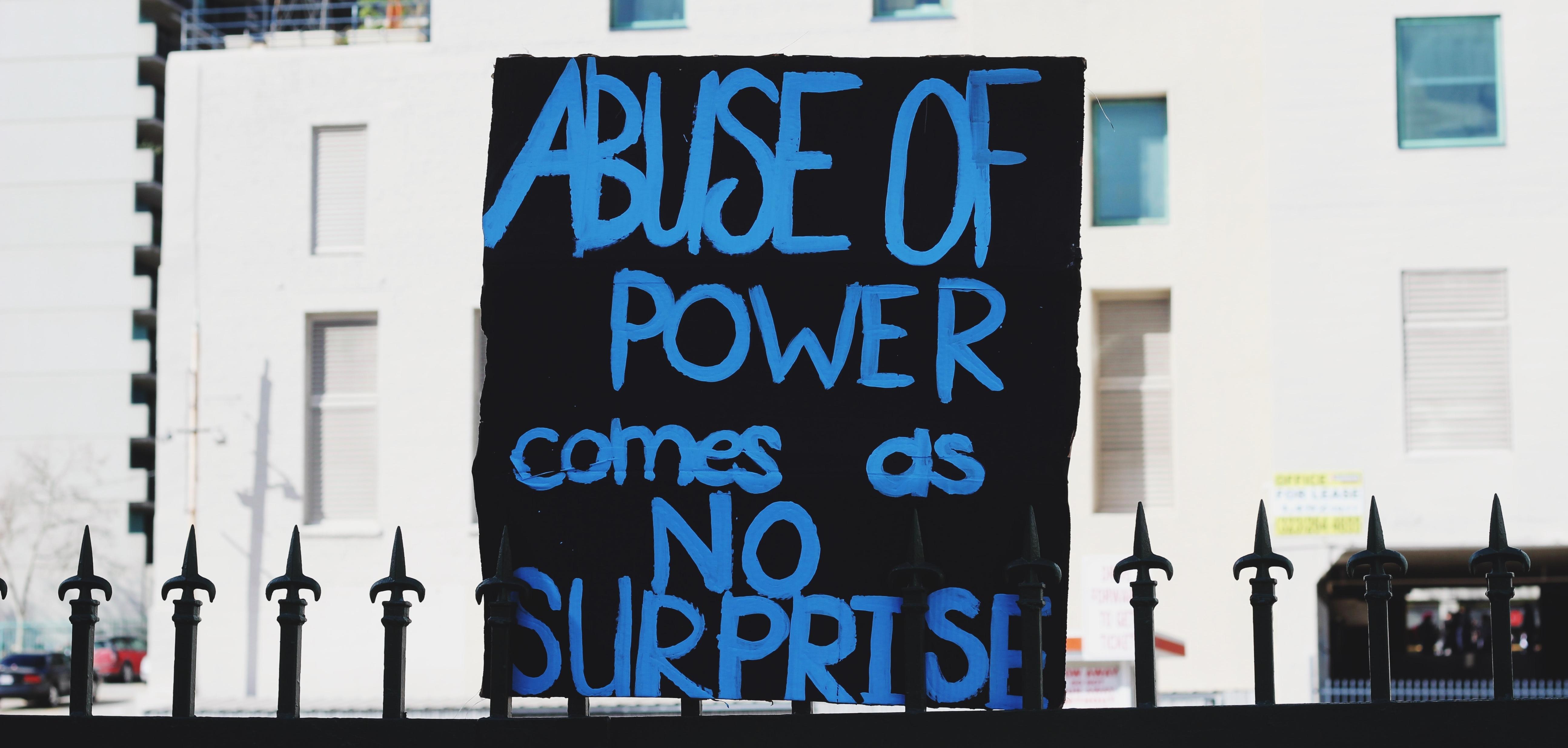 A black sign that says "Abuse of power comes as no surprise."
