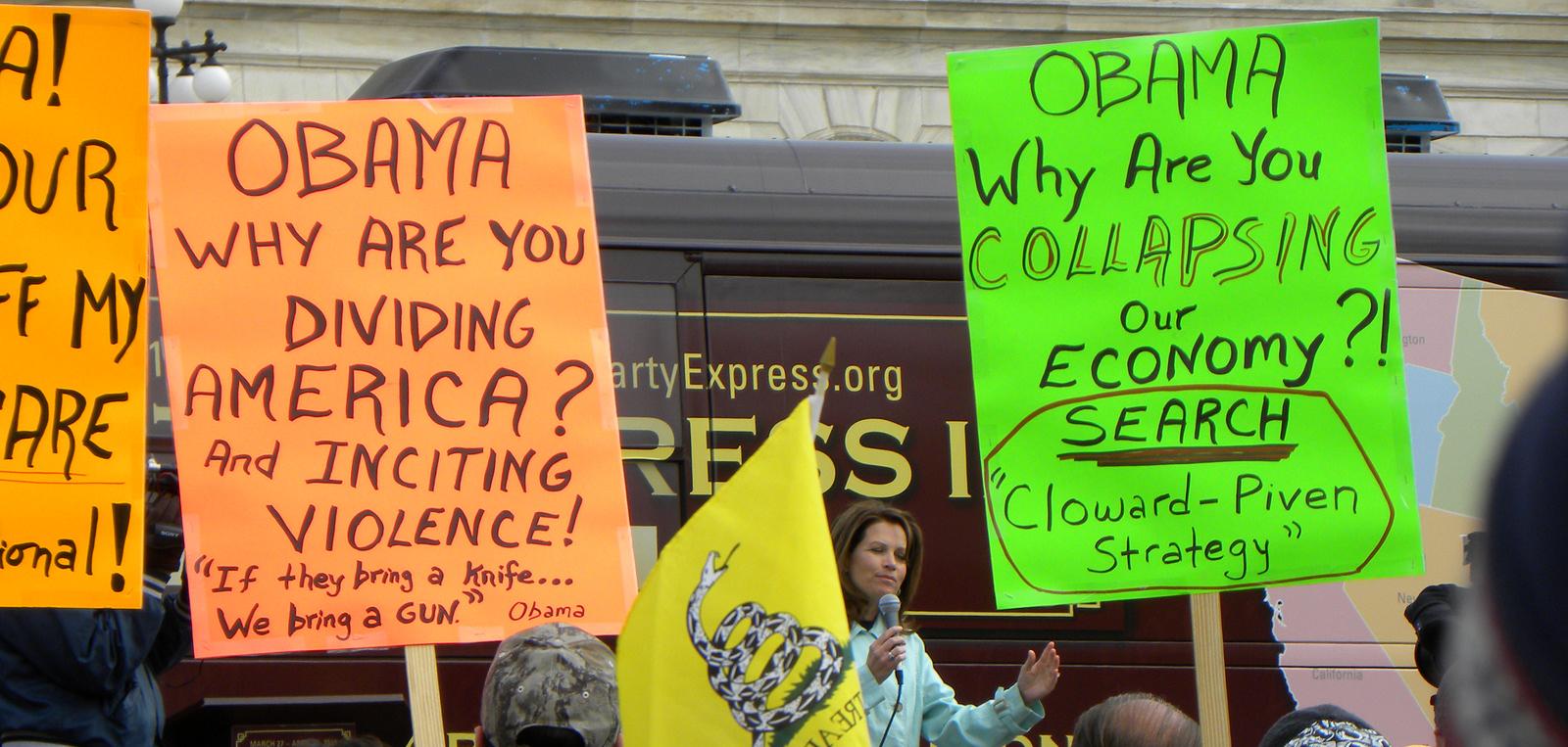 Protesters with signs that say "Obama why are you dividing America? And inciting violence!" and "Obama Why are you collapsing our economy?"