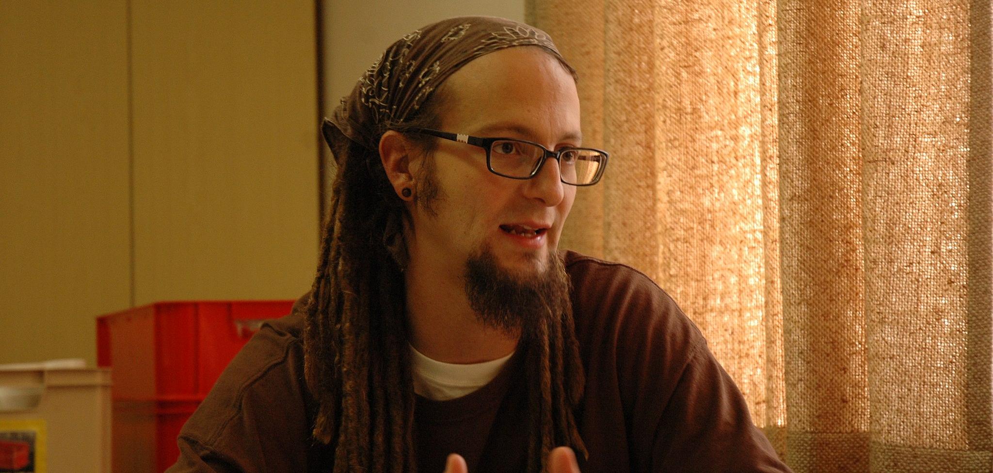 A White man wearing a sweater, with glasses and a bandana and dreadlocks.
