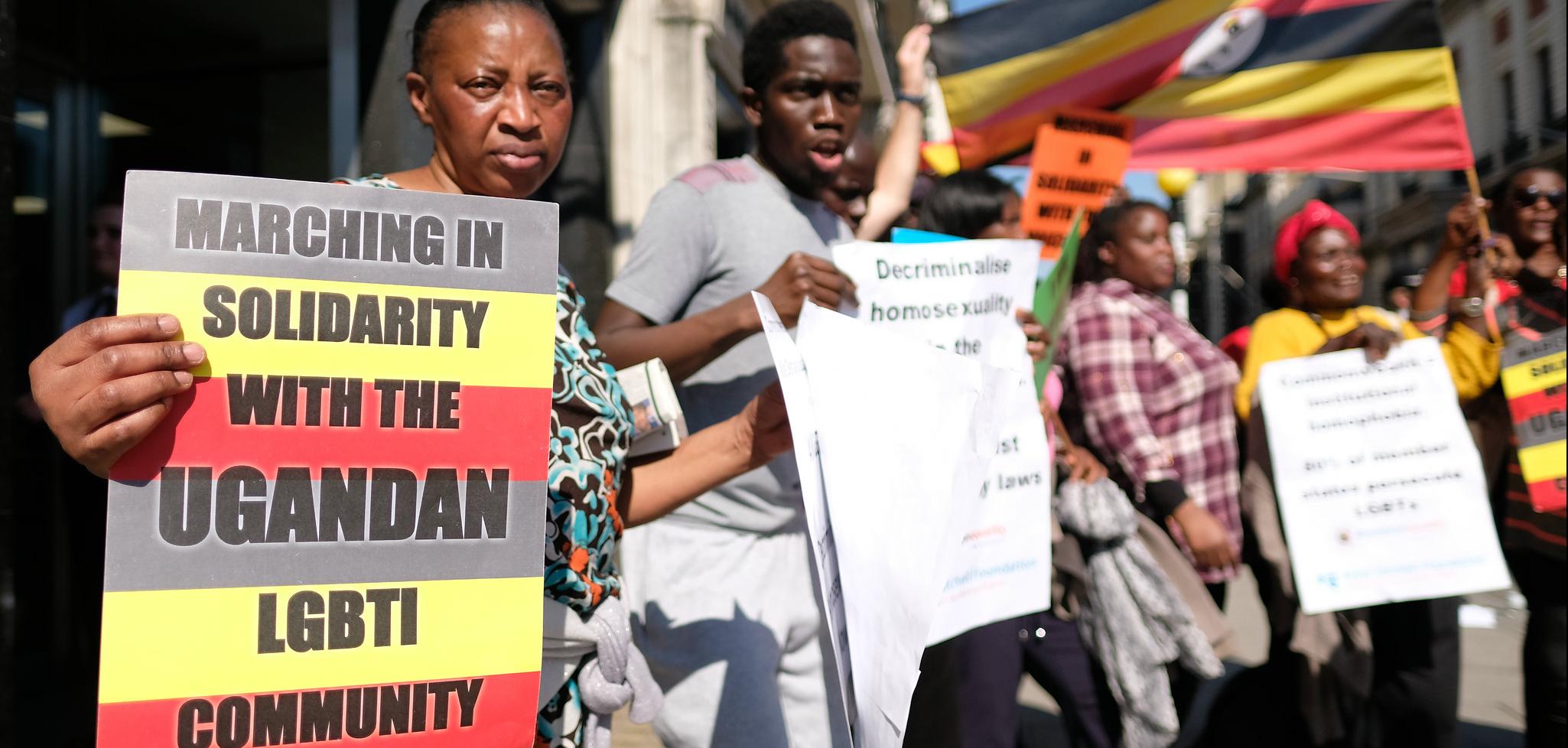 A woman in the front of the frame holding a sign that reads "marching in solidarity with the Ugandan LGBTI Community"