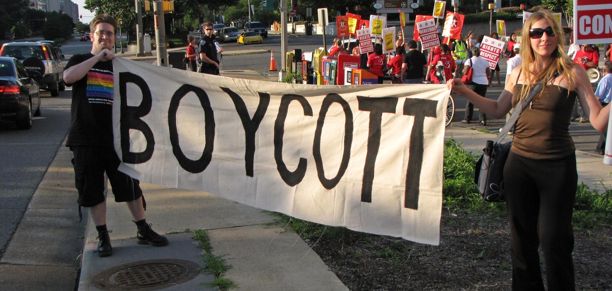 Two people holding a sign that says "Boycott" at a protest