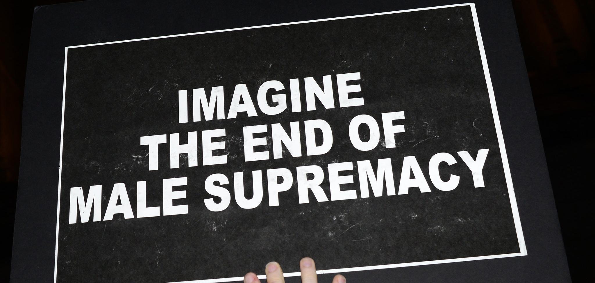 A black sign with the words "imagine the end of male supremacy"