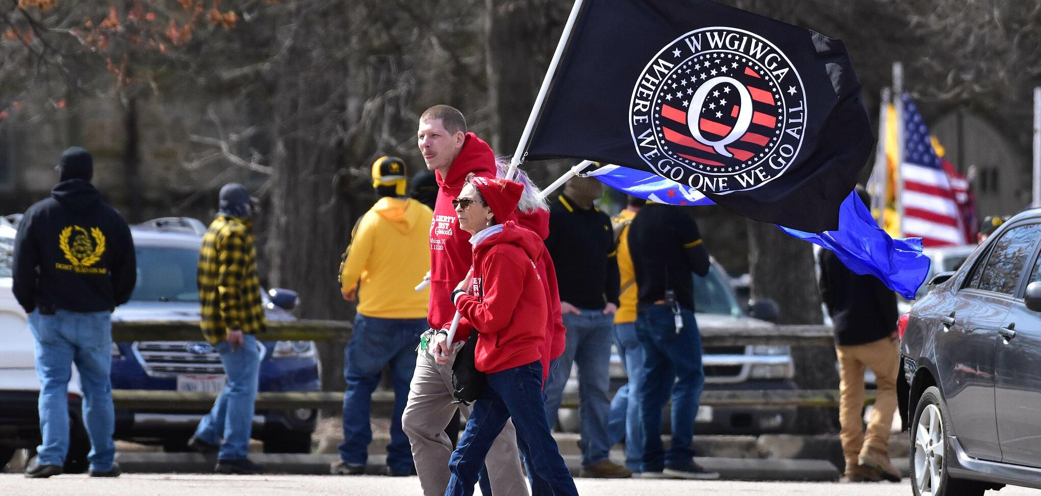Two people in red hoodies carrying a QAnon flag