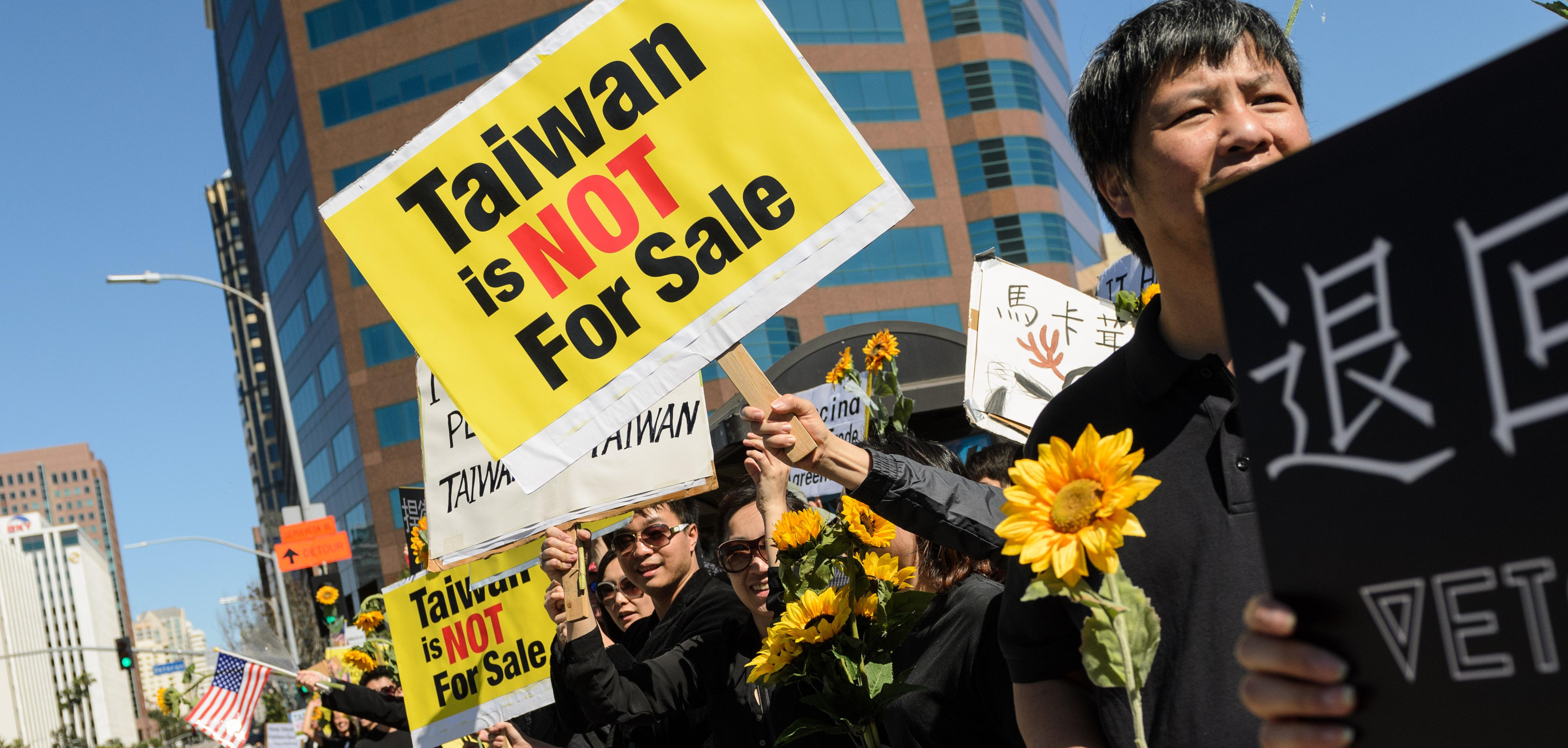 people standing in a row holding sunflowers. A sign says "Taiwan is not for sale."