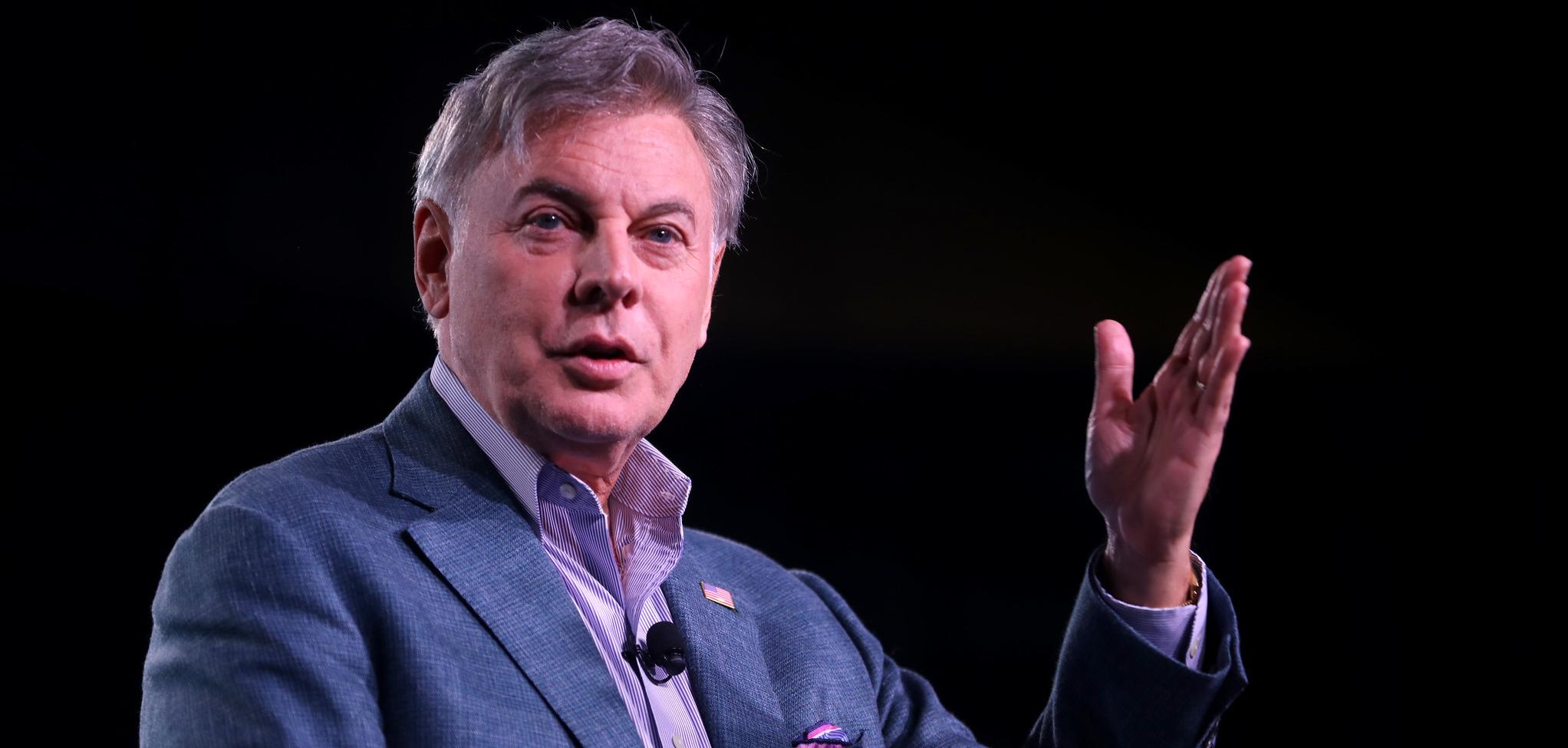 A man in a suit talking with his hand raised.