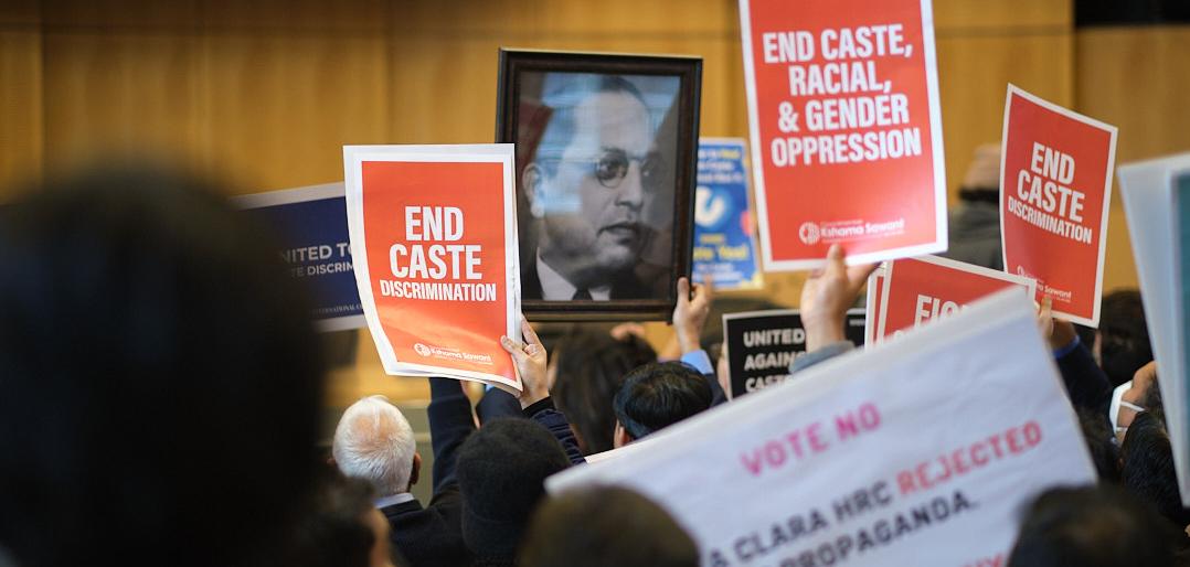 People holding banners that say "End Caste Discrimintaion" and "End Caste, Racial, And Gender Opression" and a picture of Dr. Ambedkar.