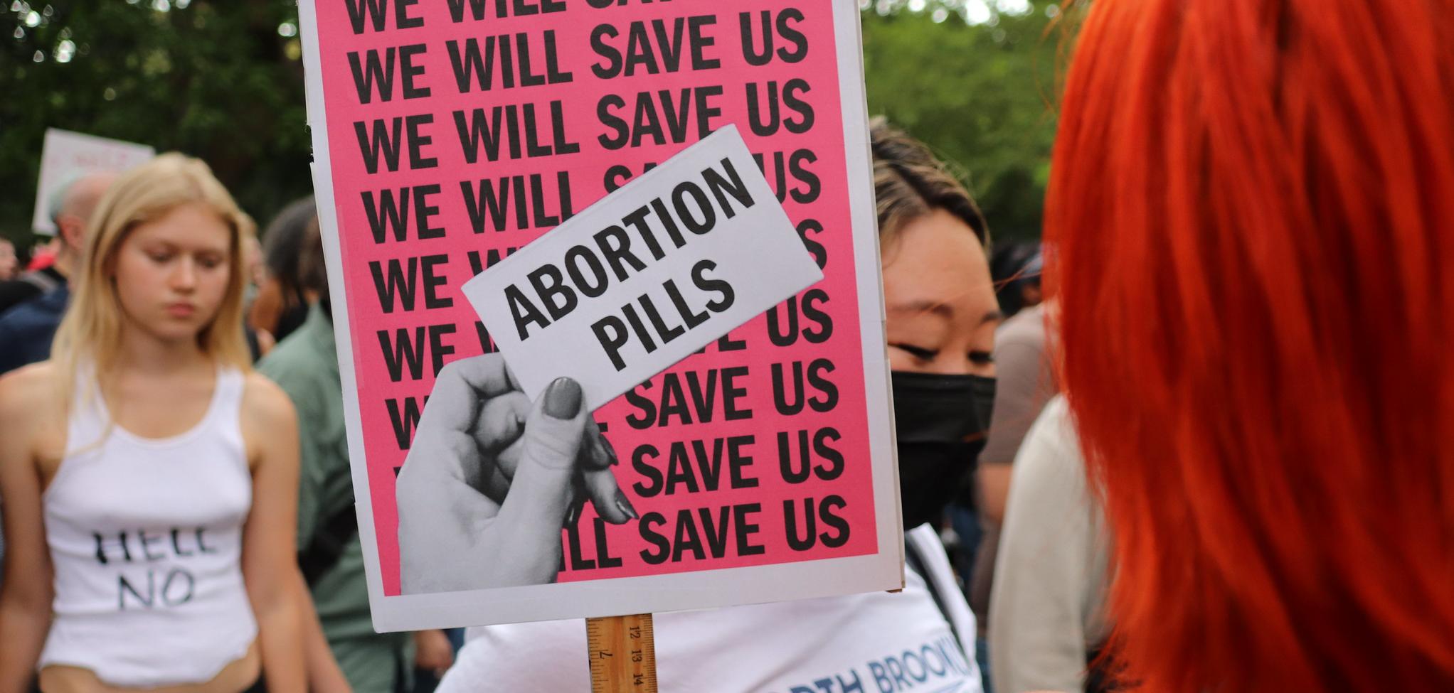 a sign that reads "We will save us" over and over again with a hand that holds a paper that says "Abortion Pills"
